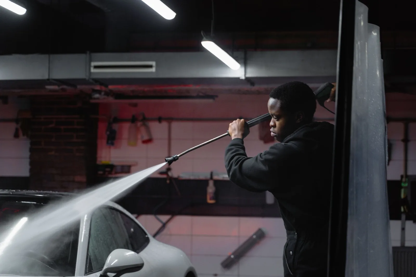 A man uses a high-pressure hose to wash a car in an indoor garage setting. Photo by Tima Miroshnichenko on Pexels