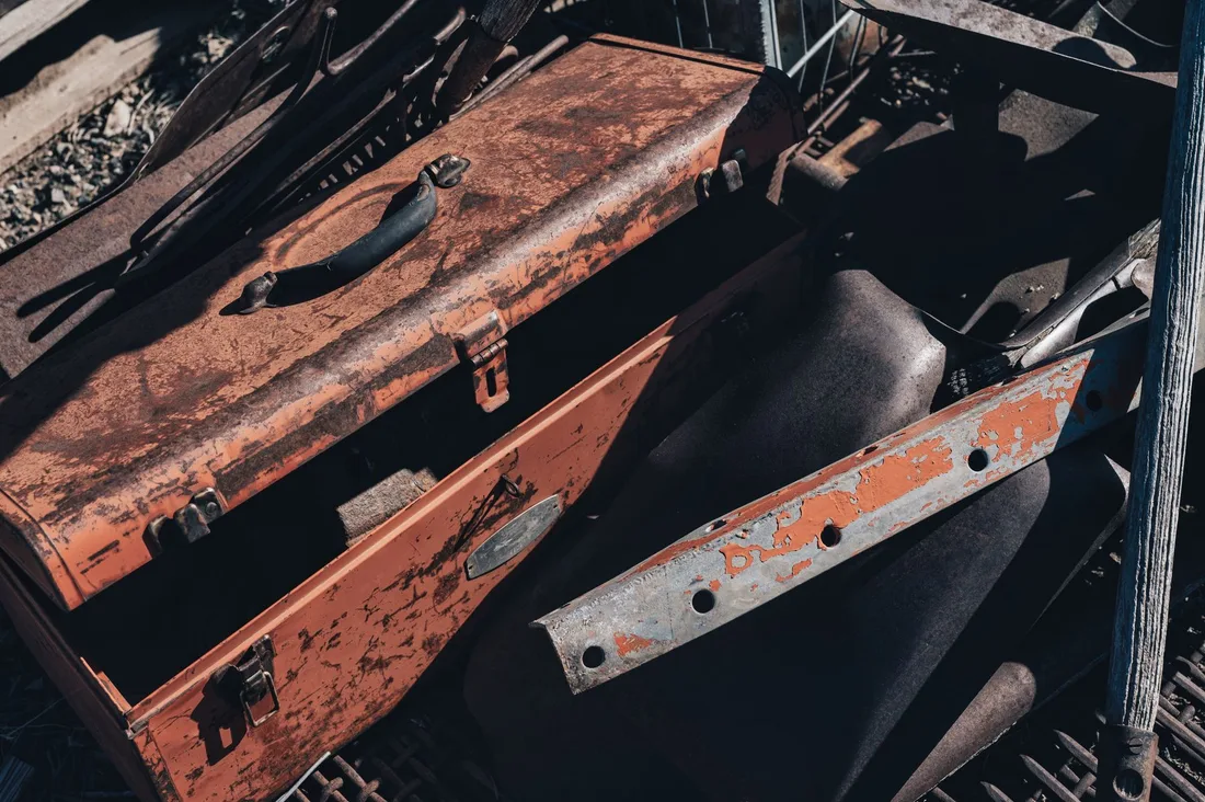A vintage rusty toolbox amidst scrap metal pieces in a junkyard under sunlight. Photo by Alfo Medeiros on Pexels