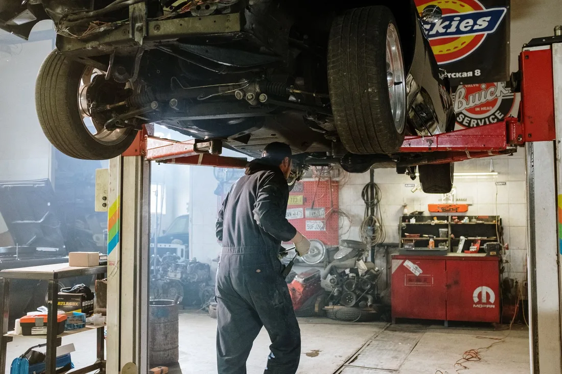 Mechanic repairing a vehicle in a busy workshop with various automotive tools. Photo by cottonbro studio on Pexels