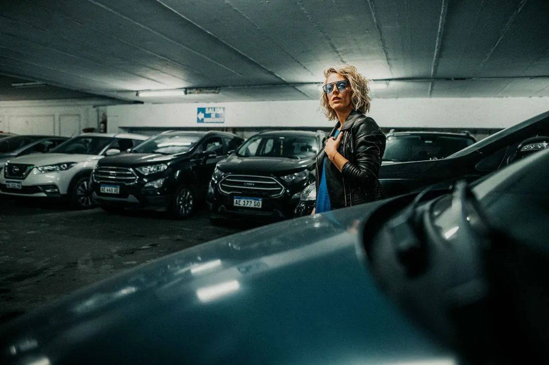 Woman standing among parked cars inside a multi-level parking garage. Photo by Gera Cejas on Pexels