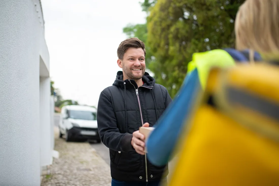 Smiling man receives a package from a delivery person outdoors in a friendly exchange. Photo by Kampus Production on Pexels