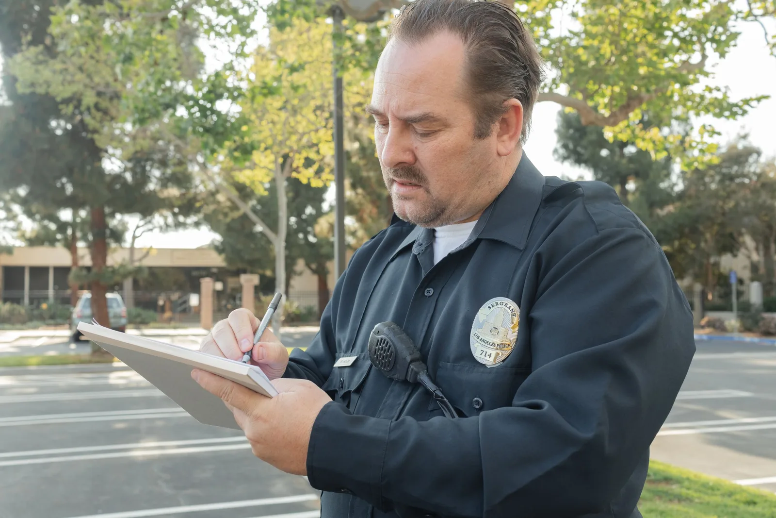 A police officer outdoors writing a report on a notepad. Trees in the background. Photo by Kindel Media on Pexels