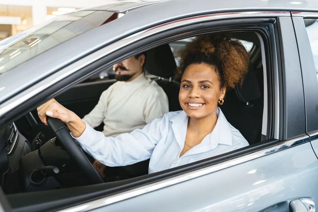 Smiling woman driver behind the wheel of a car with a passenger beside her. Photo by Antoni Shkraba on Pexels