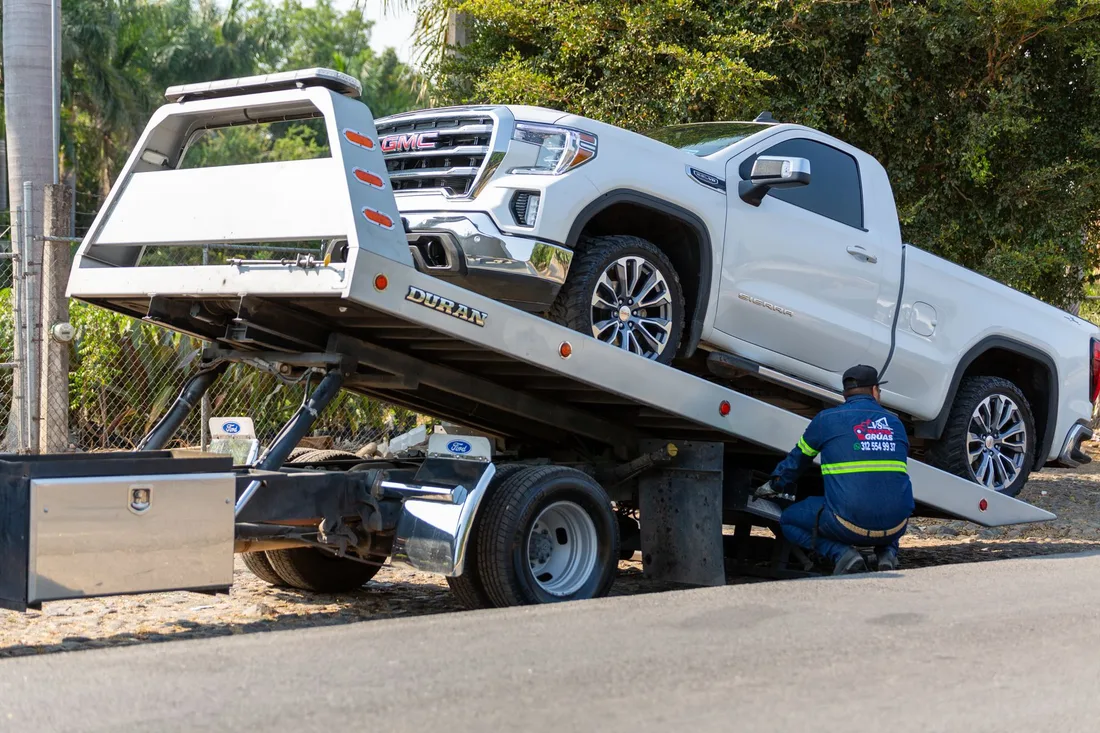 Tow truck operator loading white GMC pickup truck on street in daytime. Photo by Jonathan  Reynaga on Pexels