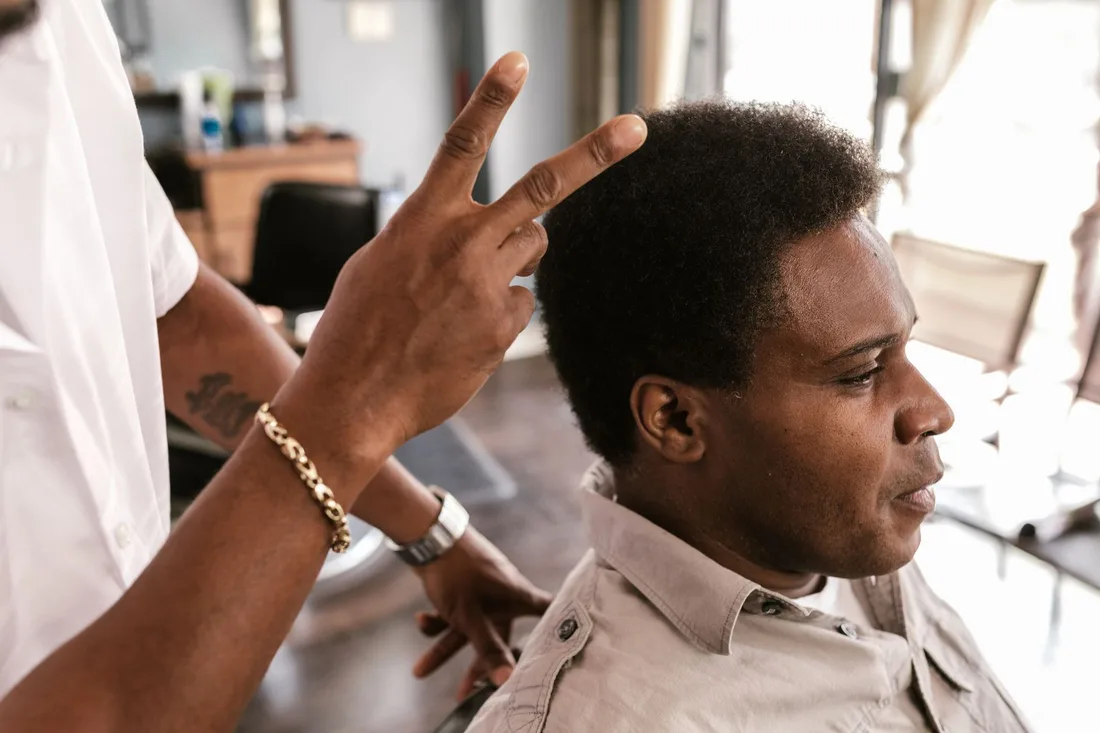 Barber styling client's afro hair in an urban barbershop, showcasing peace gesture. Photo by RDNE Stock project on Pexels