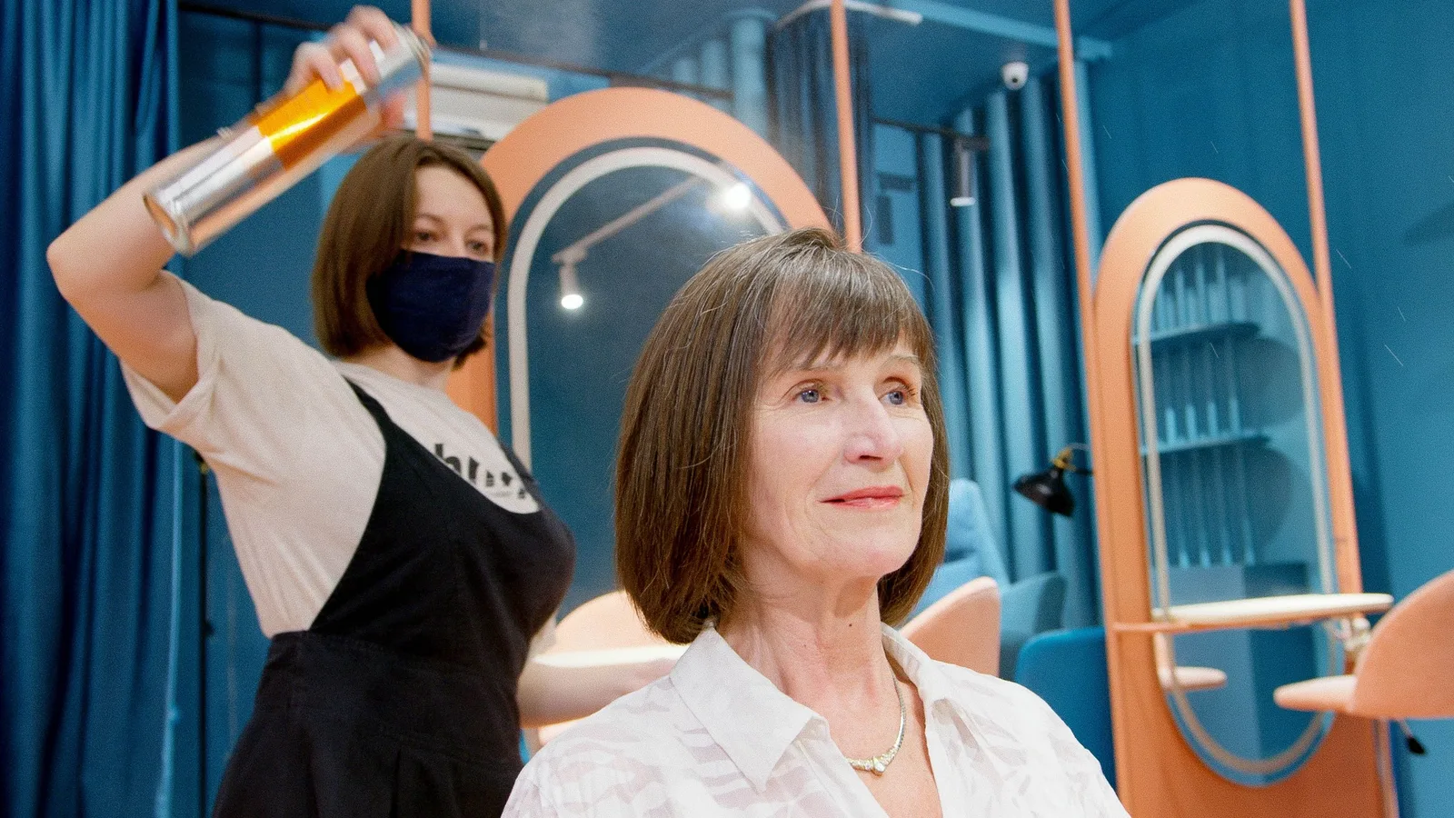 A hairstylist applies hairspray to a senior woman's new hairstyle in a modern salon. Photo by Artem Podrez on Pexels
