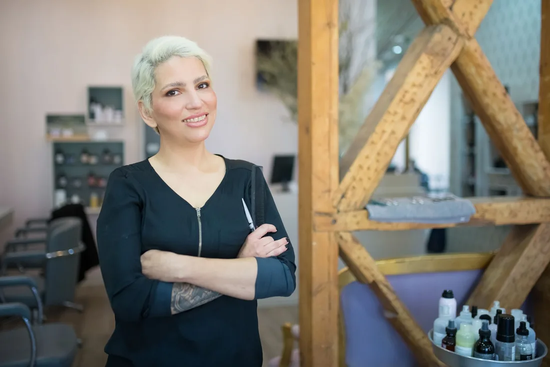 A confident female hair stylist smiling in a contemporary salon in Portugal. Photo by Kampus Production on Pexels