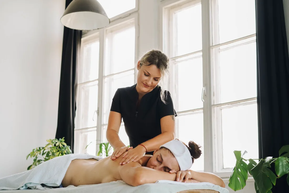 Therapist giving a client a back massage in a bright room with large windows. Photo by olia danilevich on Pexels