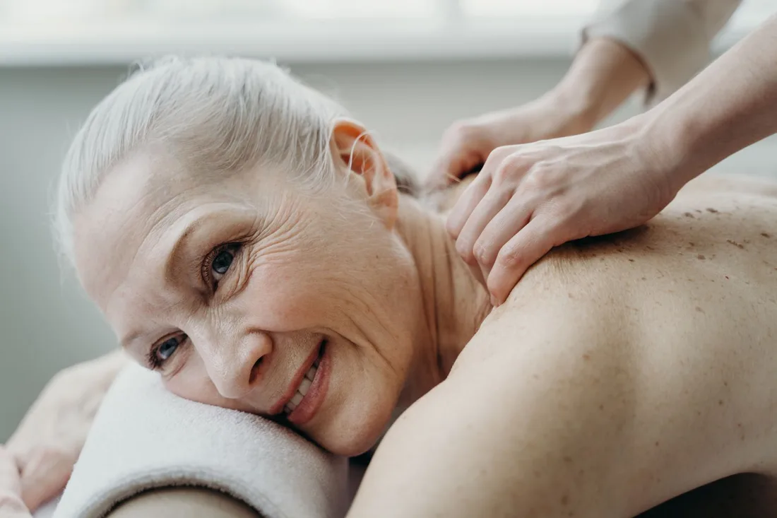 Smiling older woman resting on a massage table while receiving a shoulder massage. Photo by cottonbro studio on Pexels