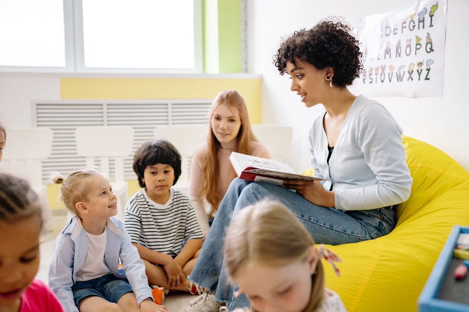 Teacher reading a picture book to a group of children in a bright classroom. Photo by Yan Krukau on Pexels