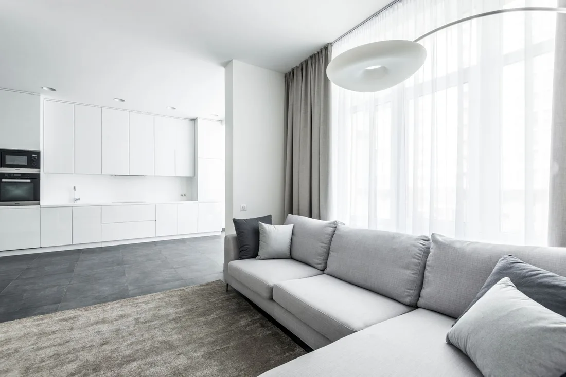 Bright living room with grey sofa, rug and tall windows with curtains. Photo by Max Vakhtbovych on Pexels