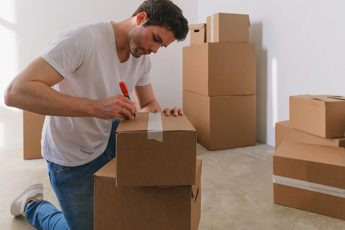 Man taping and labelling moving boxes in an empty bright apartment. Photo by SHVETS production on Pexels