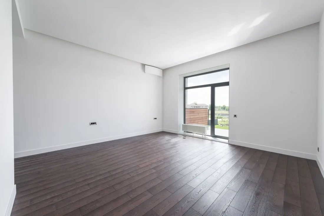 Clean empty apartment room with white walls, dark wood floor and balcony door. Photo by Max Vakhtbovych on Pexels