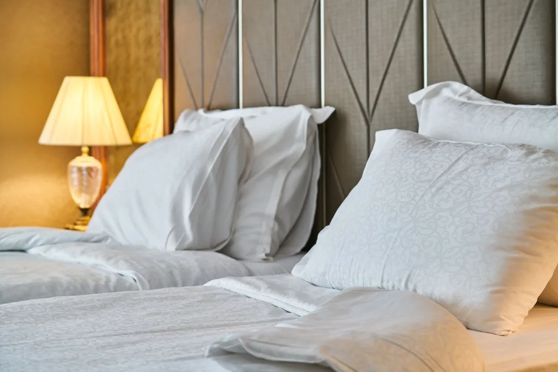 Fresh white pillows and linen on a clean bed with a padded headboard. Photo by Engin Akyurt on Pexels
