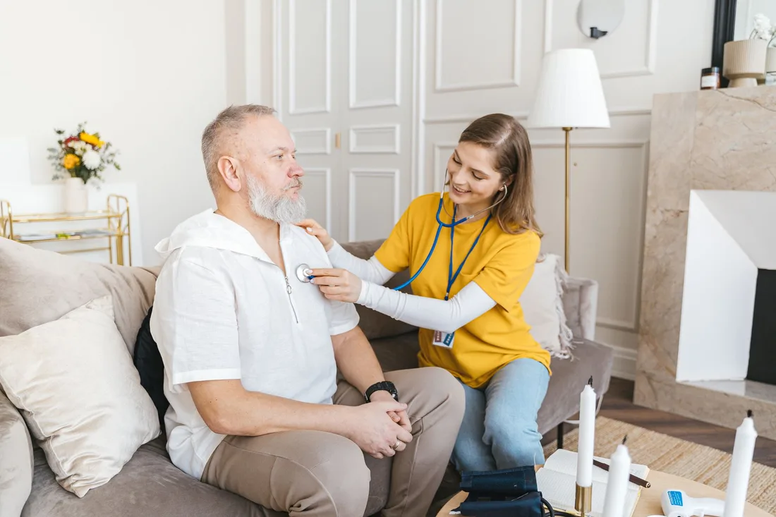 Carer sitting beside an older man on a sofa in a bright living room in Australia. Photo by Antoni Shkraba on Pexels