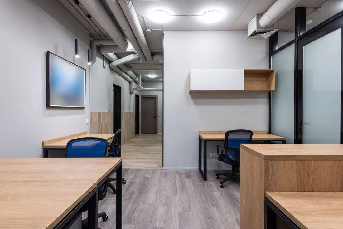 Tidy office room with wooden desks and blue chairs under bright lighting. Photo by Max Vakhtbovych on Pexels