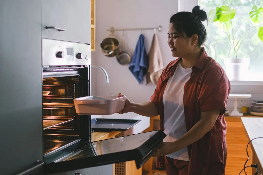 Woman taking a baking dish from a built-in oven in a bright home kitchen. Photo by Anna Shvets on Pexels