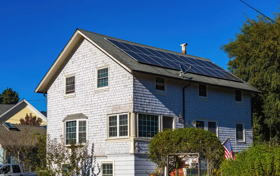 Suburban house with solar panels on the roof under a blue sky. Photo by Robert So on Pexels
