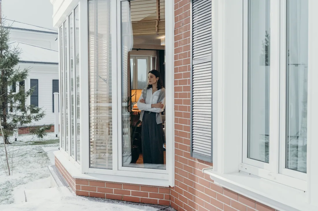 Woman standing at an open bay window of a bright suburban house. Photo by cottonbro studio on Pexels