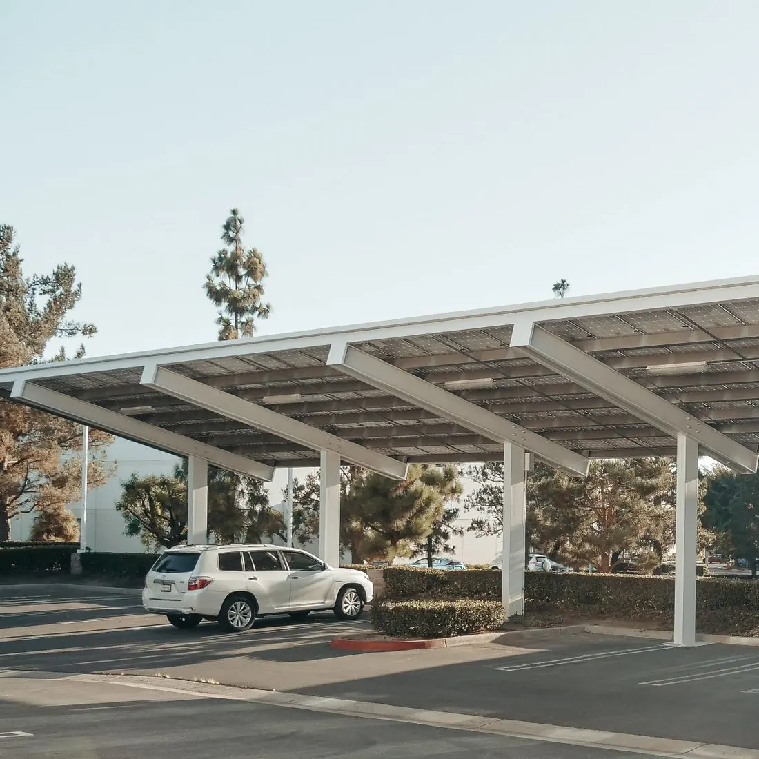 Side view of a solar canopy over a commercial parking area, with a white SUV parked beneath it and trees behind. Photo by Kindel Media on Pexels