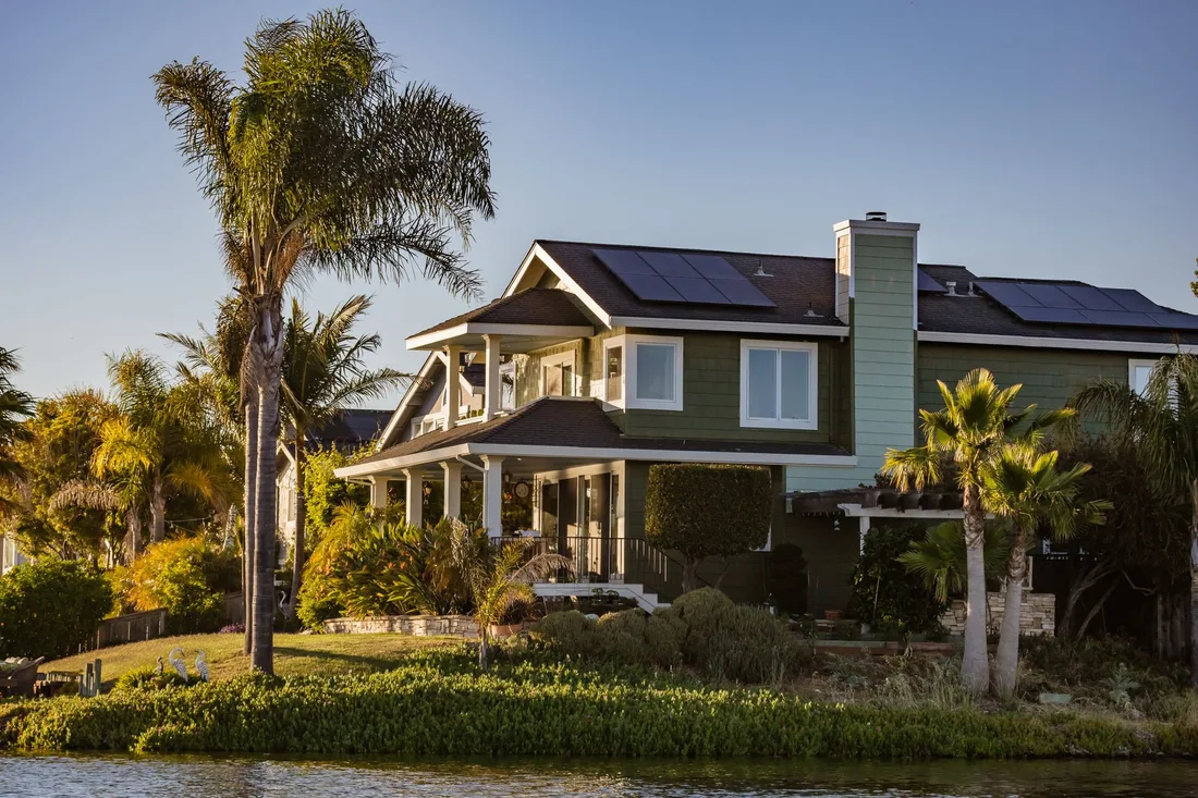 Sunny home with solar panels on the roof and palm trees in front. Photo by Robert So on Pexels