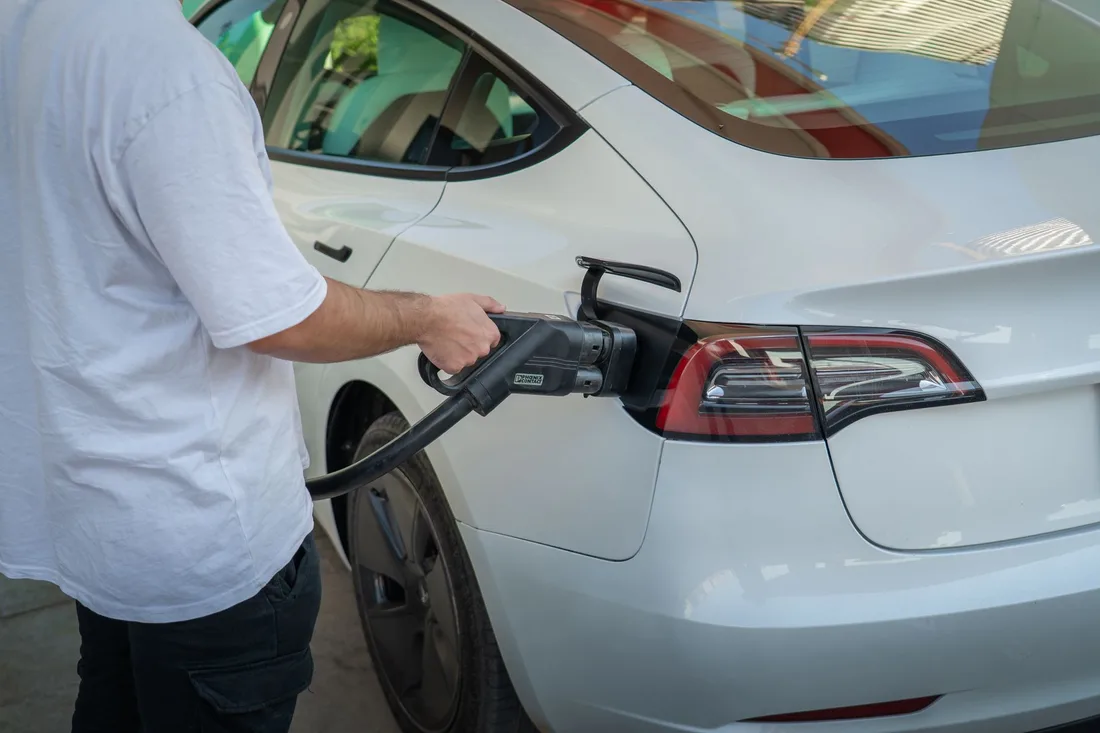 Person plugging a charging cable into the rear port of a white electric car. Photo by 04iraq on Pexels