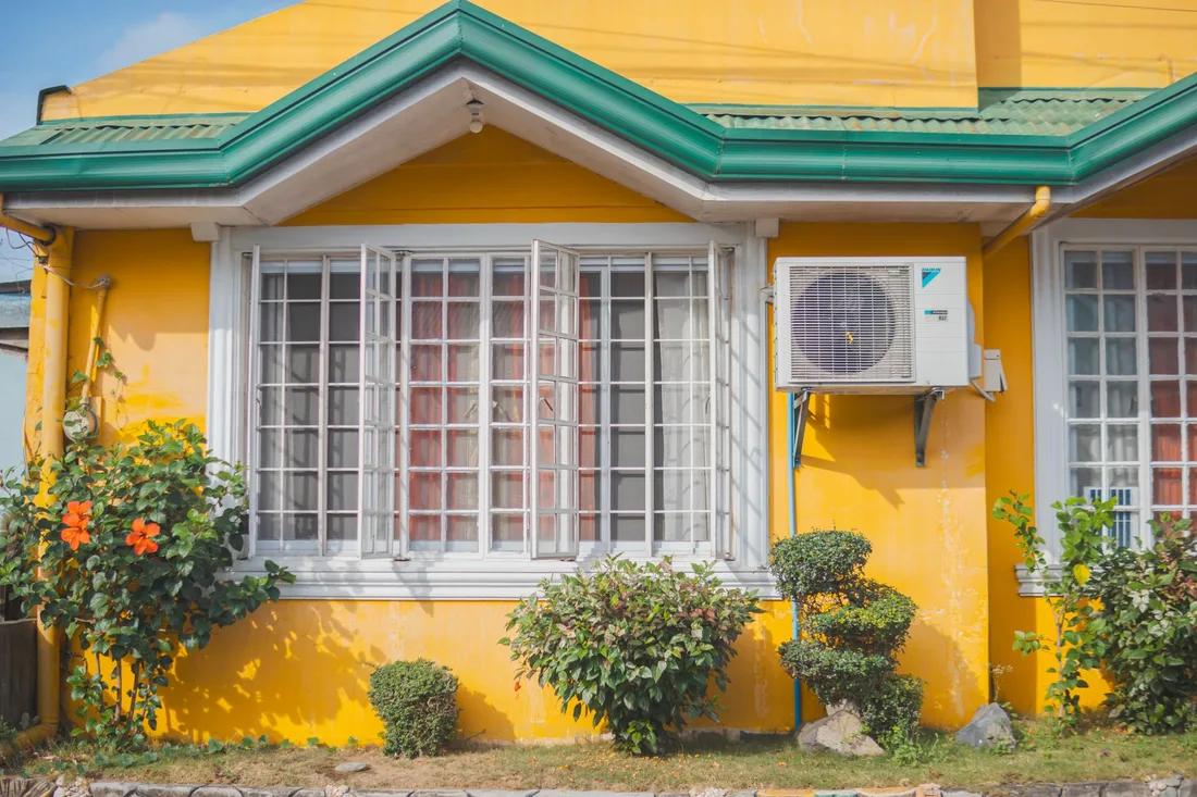 Yellow house with a wall mounted heat pump unit beside a window. Photo by Nothing Ahead on Pexels