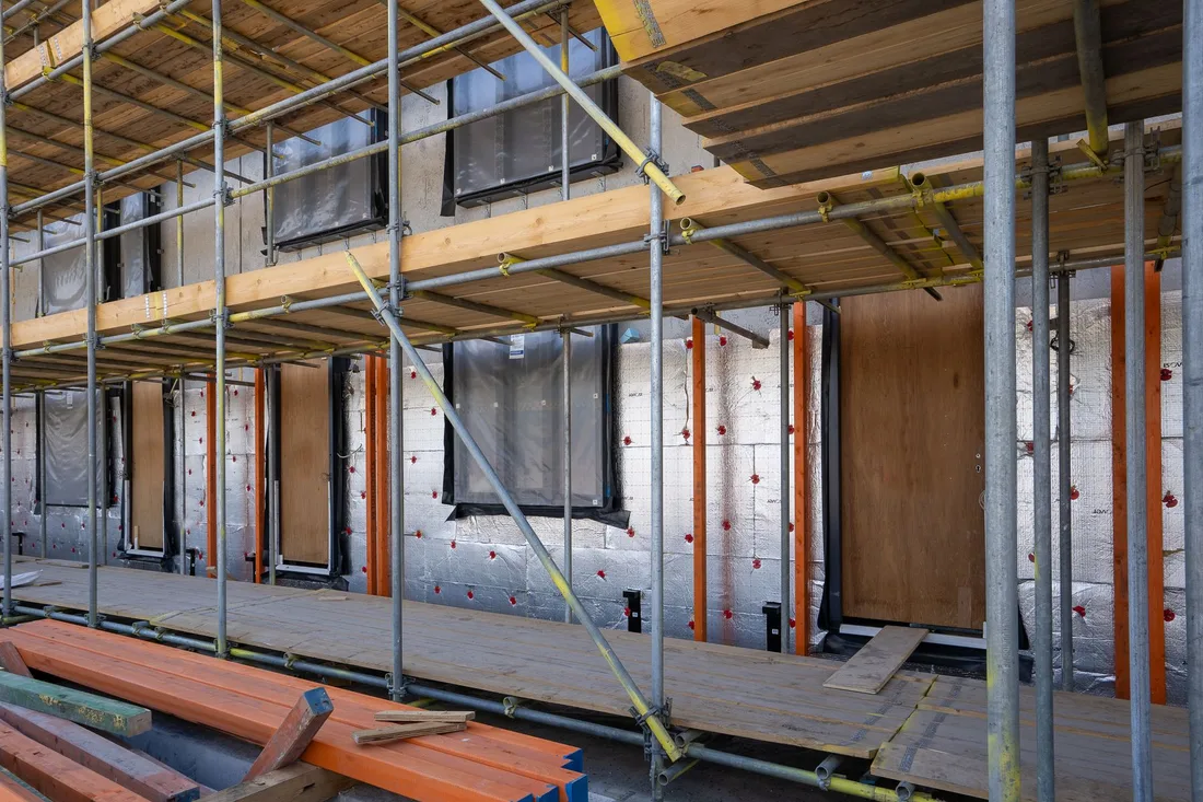 Building exterior wrapped in insulation panels behind scaffolding. Photo by Mike van Schoonderwalt on Pexels