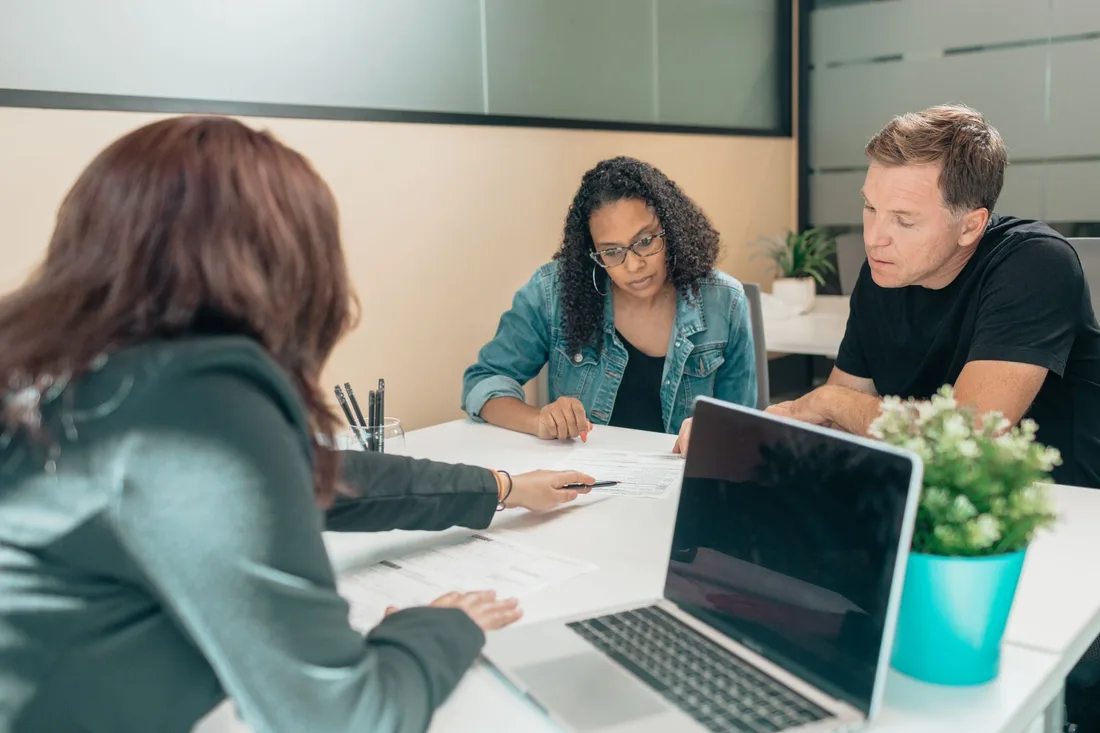Customers meeting a bank advisor at a table with a laptop in a bright branch. Photo by Kindel Media on Pexels