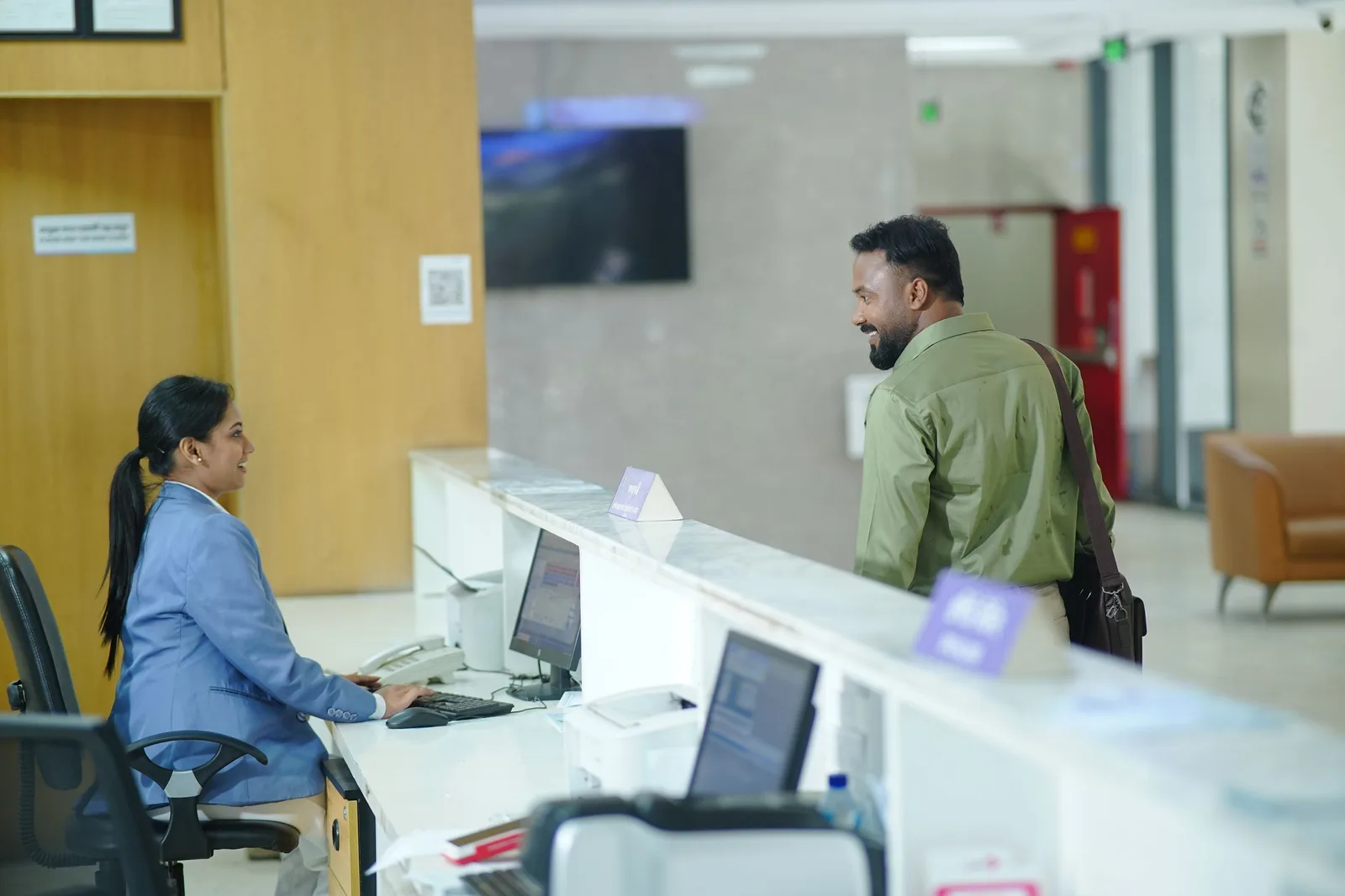 Bank teller at a branch counter assisting a customer approaching the desk. Photo by FAKHRUL HASSAN on Pexels