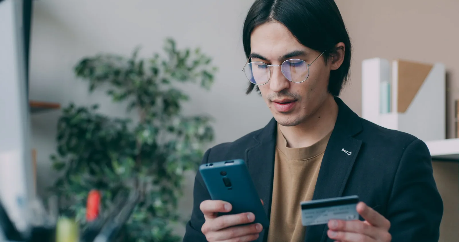 Businessman in office attire using a smartphone and holding a credit card, focusing on online payment process. Photo by Vitaly Gariev on Pexels