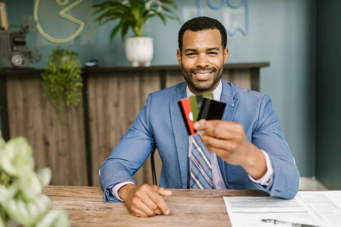 Smiling African American man in a suit holding credit cards at a business desk. Photo by RDNE Stock project on Pexels