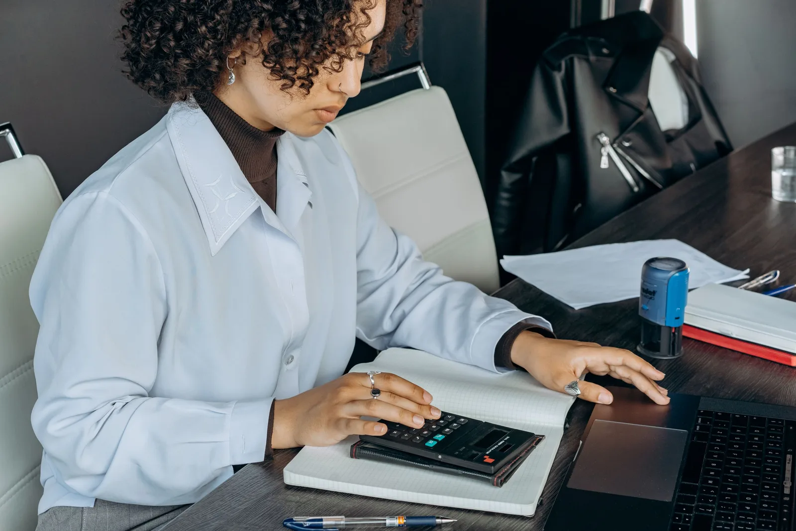 Bookkeeper in light blue shirt working at a desk with a calculator and ledger. Photo by Mikhail Nilov on Pexels