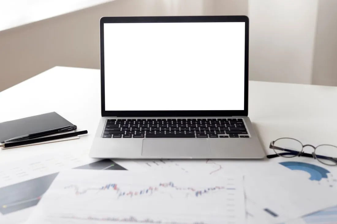 Laptop, notebook and printed charts on a white desk. Photo by Hanna Pad on Pexels