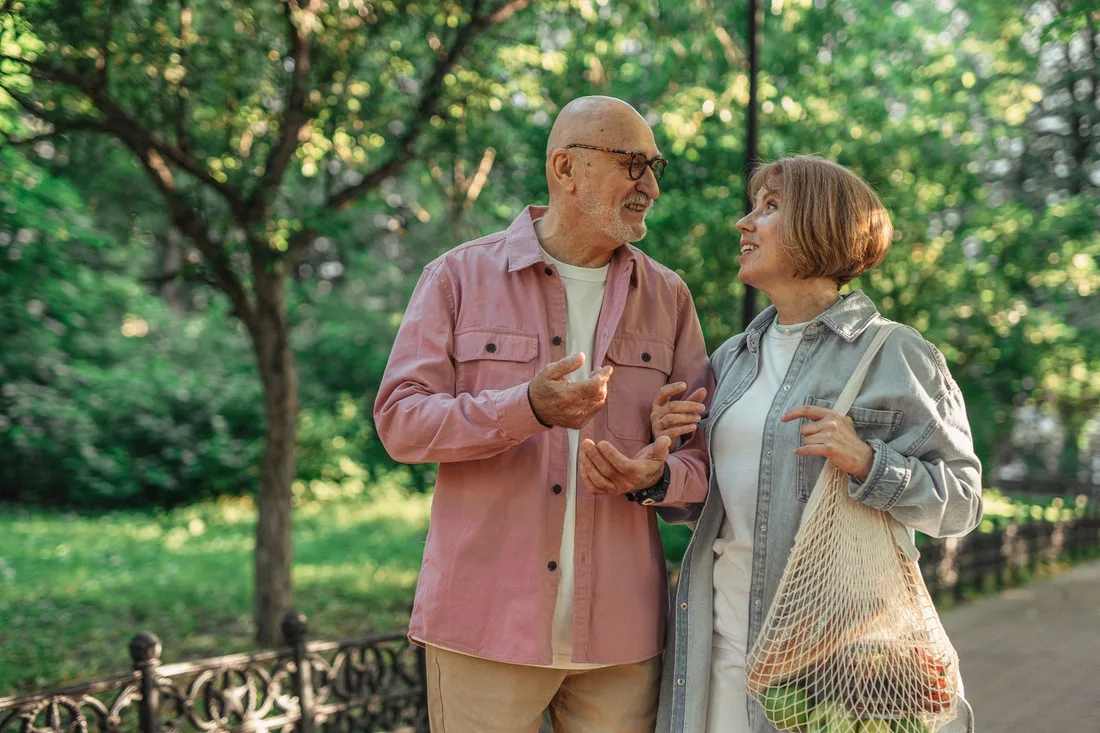 Happy retired couple chatting while walking in a green park. Photo by SHVETS production on Pexels