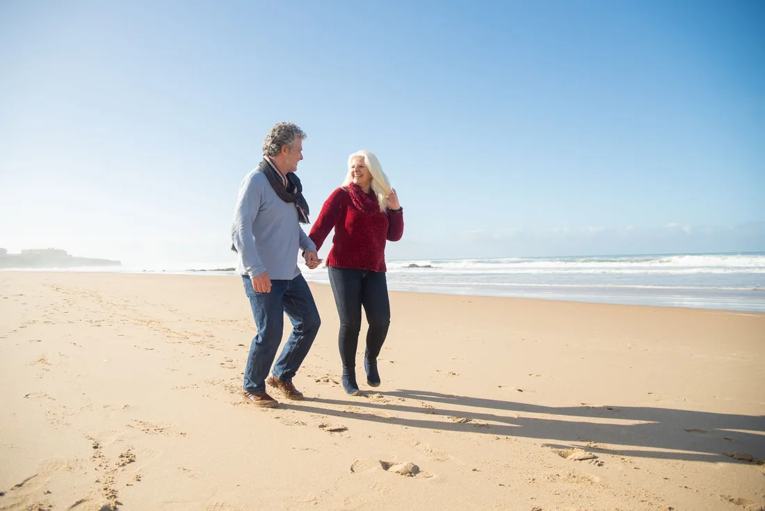 Retired couple holding hands while walking along a sunny beach in Australia. Photo by Kampus Production on Pexels