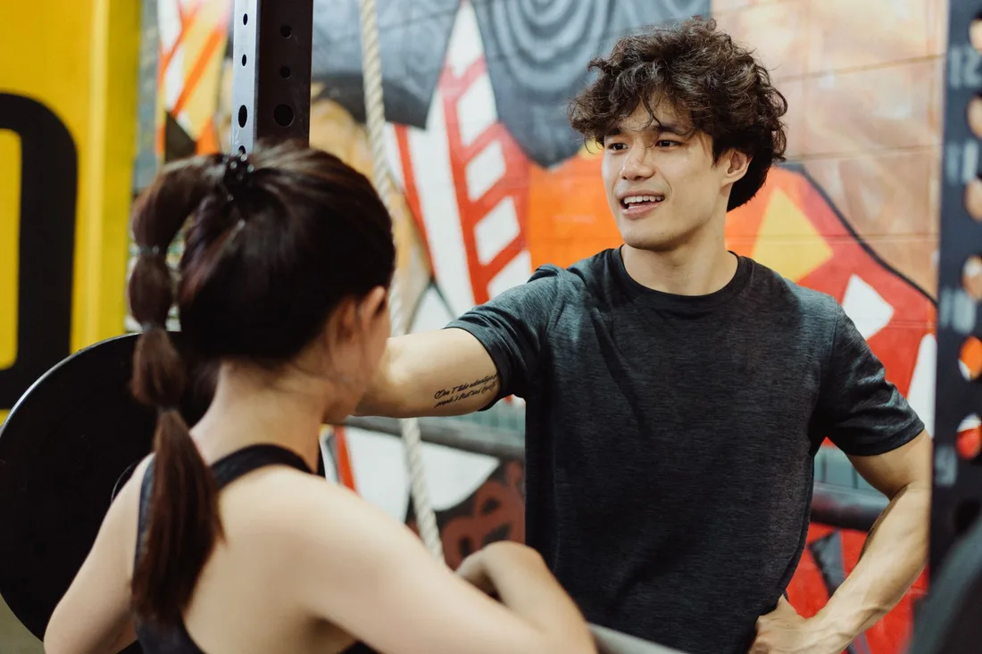 Two young adults in a gym engaging in a lively fitness discussion with a vibrant mural in the background. Photo by Ketut Subiyanto on Pexels