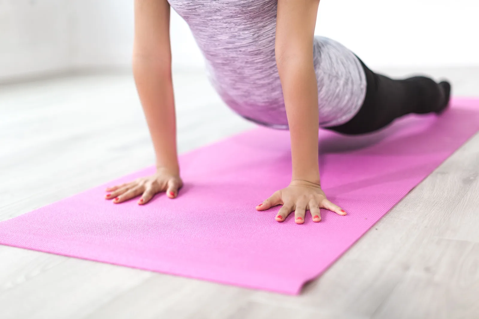 A woman performs a yoga stretch indoors on a pink mat, promoting a healthy lifestyle. Photo by Burst on Pexels