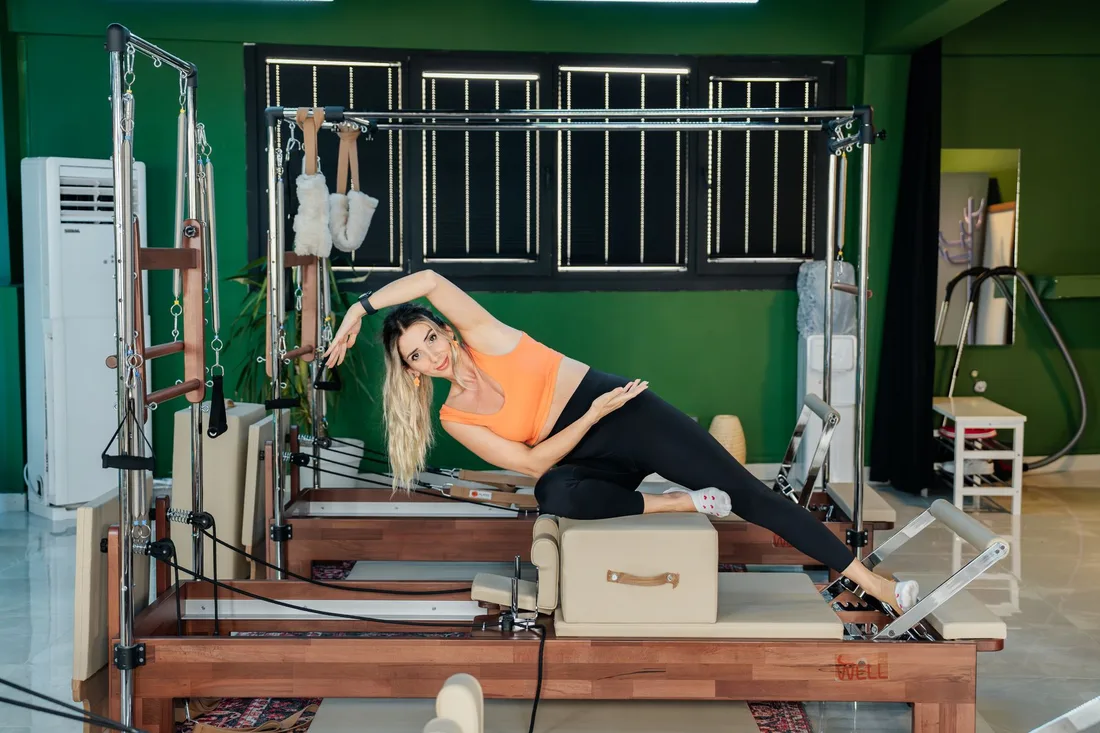 Woman performing side stretch exercise on Pilates reformer machine indoors. Photo by Ahmet Kurt on Pexels
