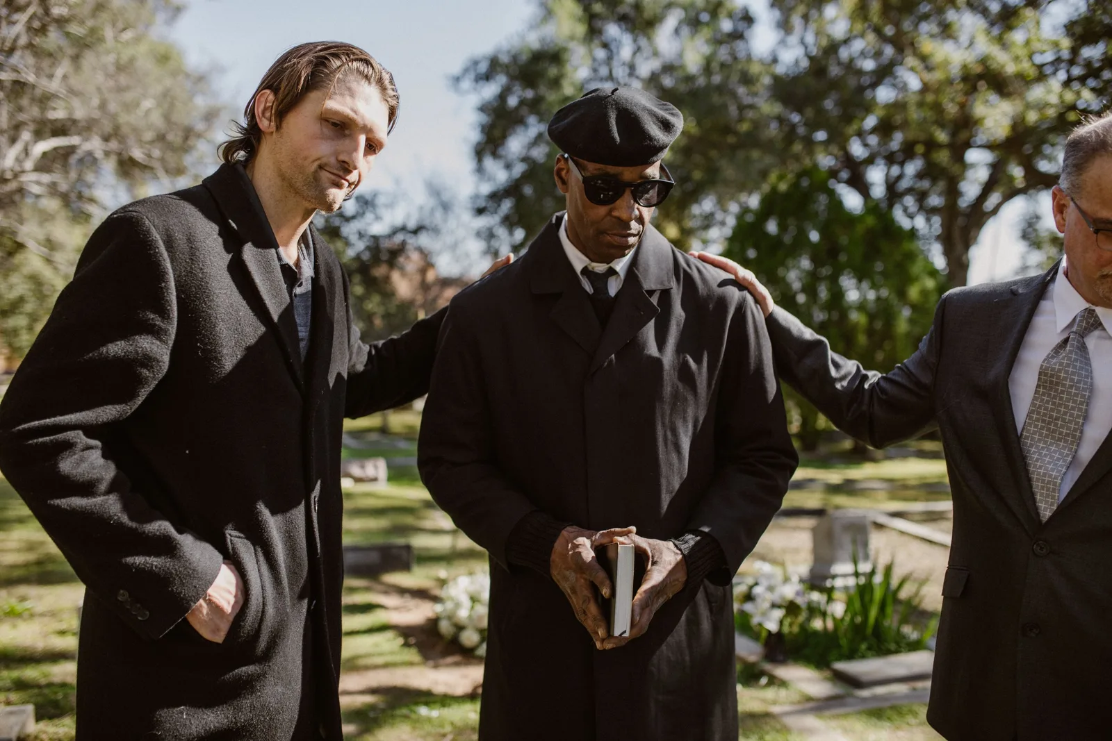 Funeral director in a dark coat and cap consoling a mourner in a quiet cemetery. Photo by RDNE Stock project on Pexels