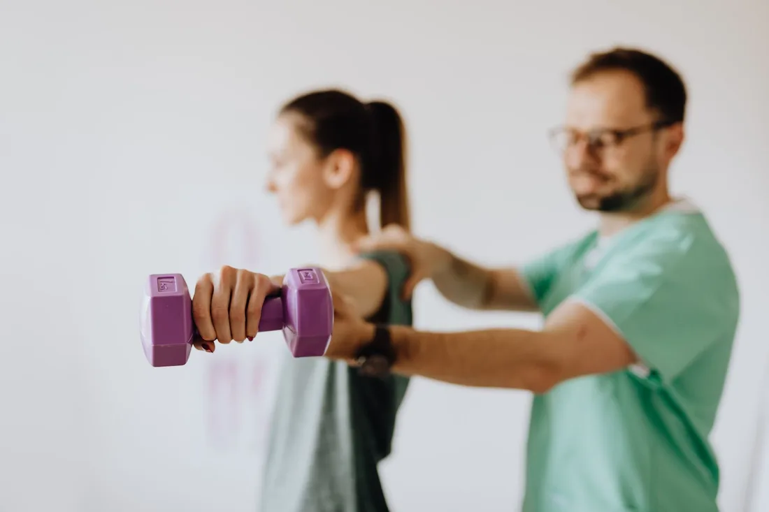 Therapist guiding a patient through a dumbbell exercise in a rehabilitation clinic. Photo by https://kaboompics.com/ on Pexels