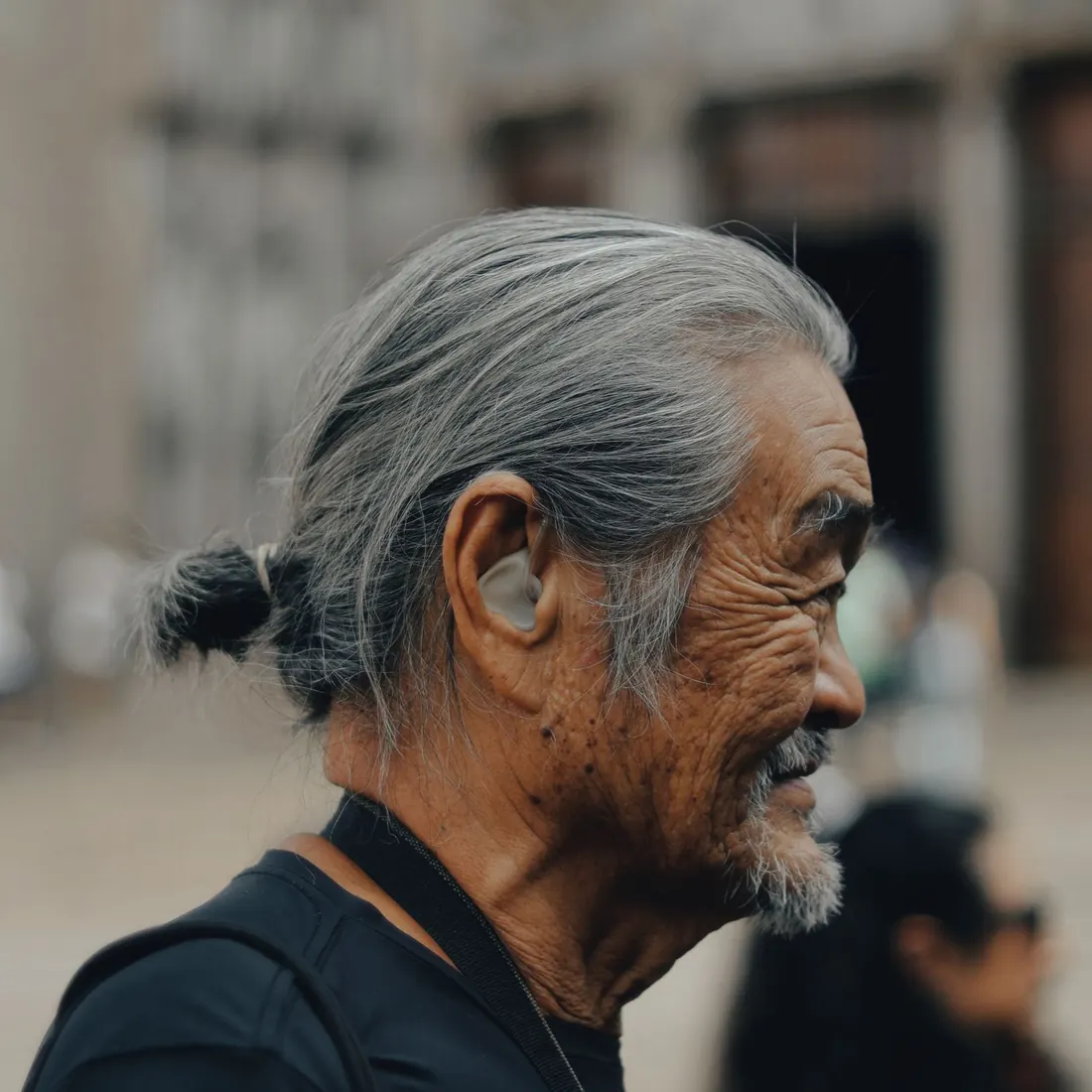 Close profile of a senior man with a grey ponytail and a small in-the-ear hearing aid, outdoors. Photo by Thedollasyn on Pexels