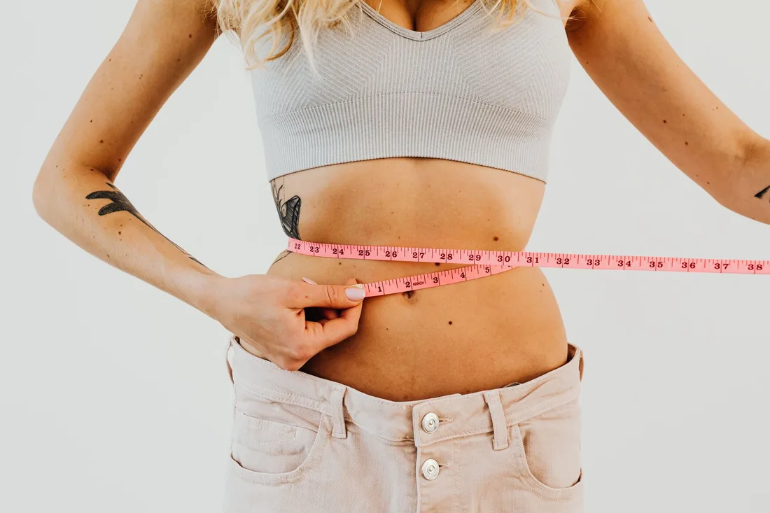 Woman in a light sports top measuring her waist with a tape measure. Photo by https://kaboompics.com/ on Pexels