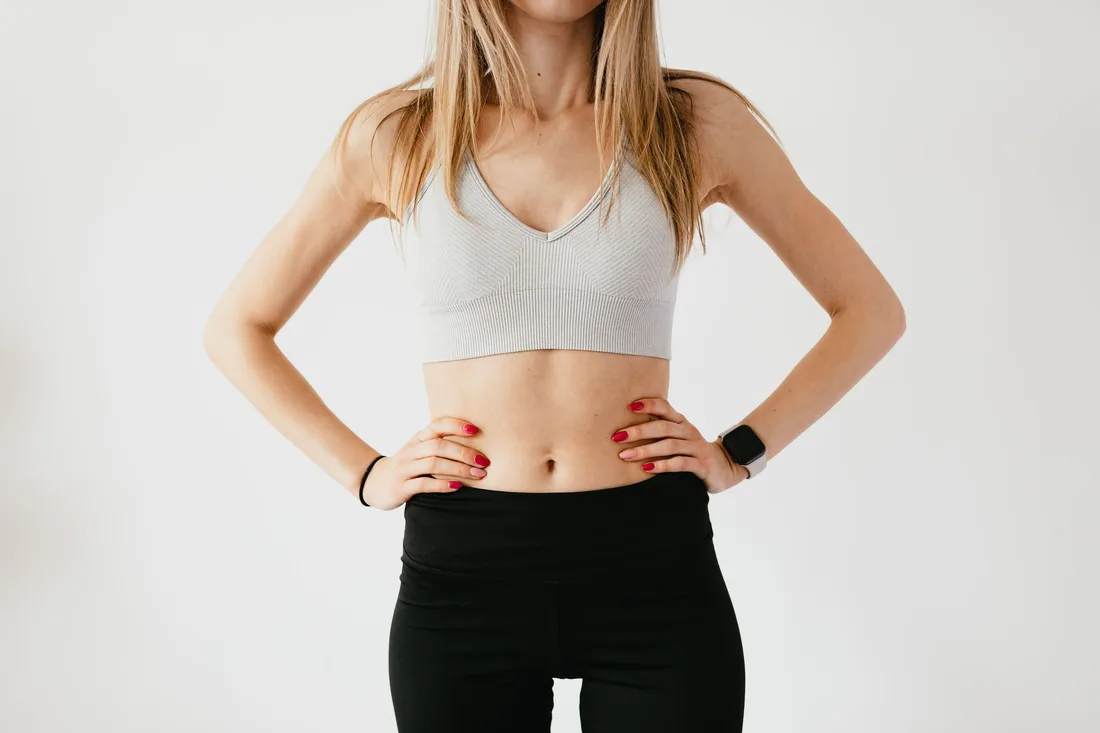 Woman in white sports top and black leggings standing with hands on her hips. Photo by https://kaboompics.com/ on Pexels