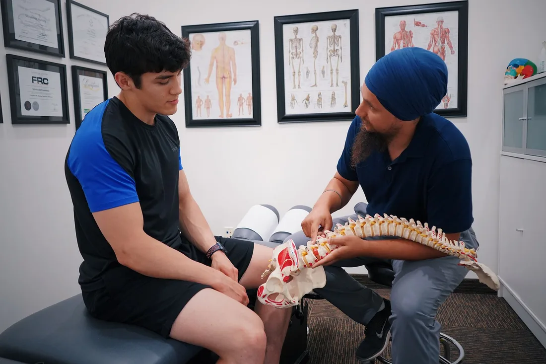 Chiropractor explaining a spine model to a patient in a clinic with anatomy posters. Photo by World Sikh Organization of Canada on Pexels