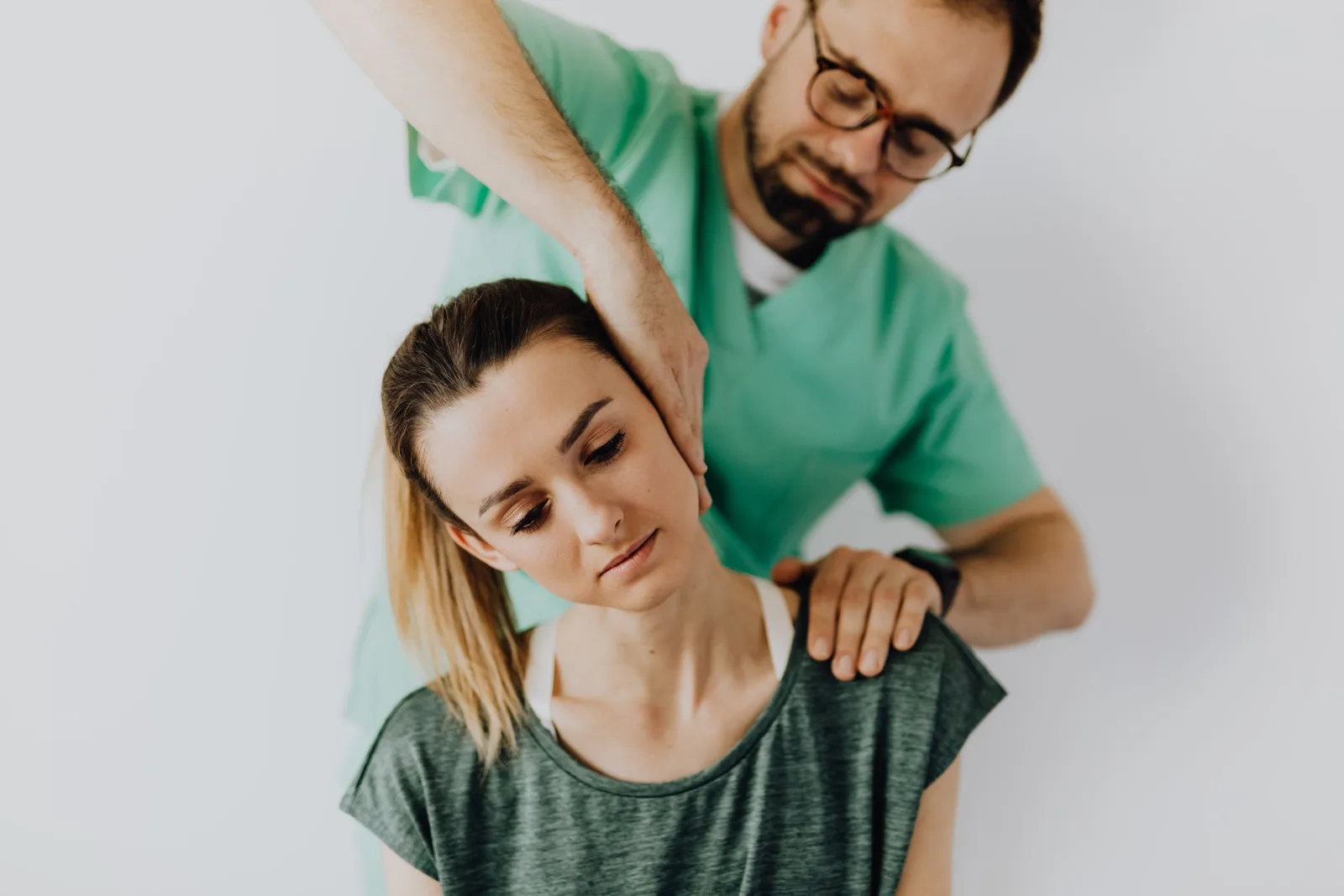 Chiropractor in green scrubs adjusting a female patient's neck and shoulders. Photo by https://kaboompics.com/ on Pexels