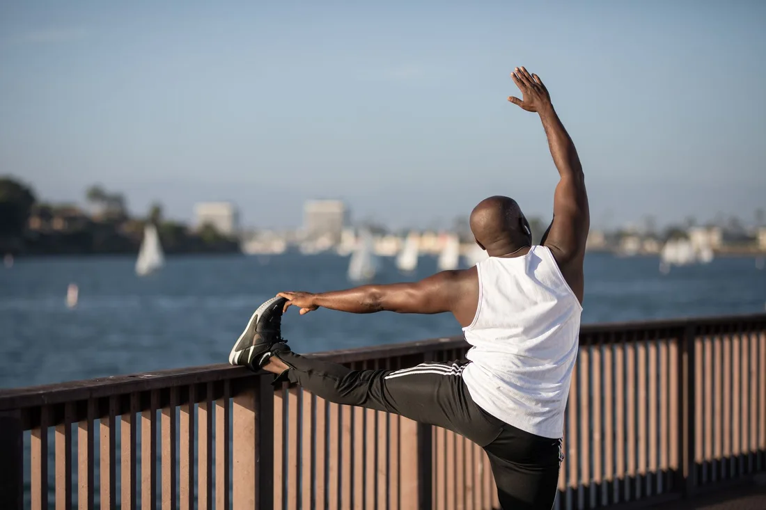 Man stretching his back and arms beside a waterfront railing in daylight. Photo by Ketut Subiyanto on Pexels