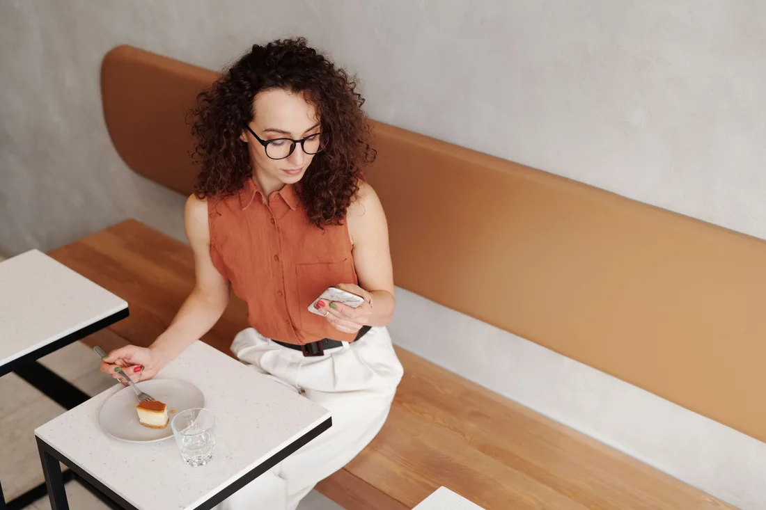 Woman with curly hair using her phone at a cafe table with a dessert. Photo by Edmond Dantès on Pexels