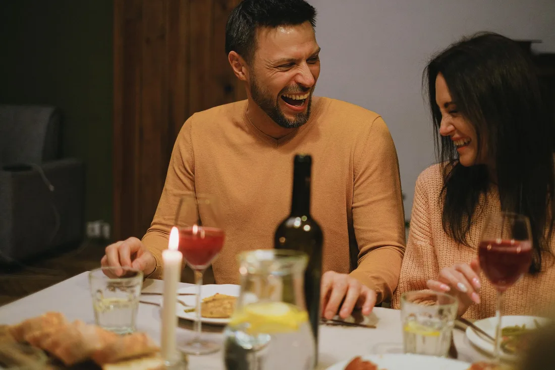 Happy couple laughing together over dinner and wine at a restaurant table. Photo by Anna Shvets on Pexels