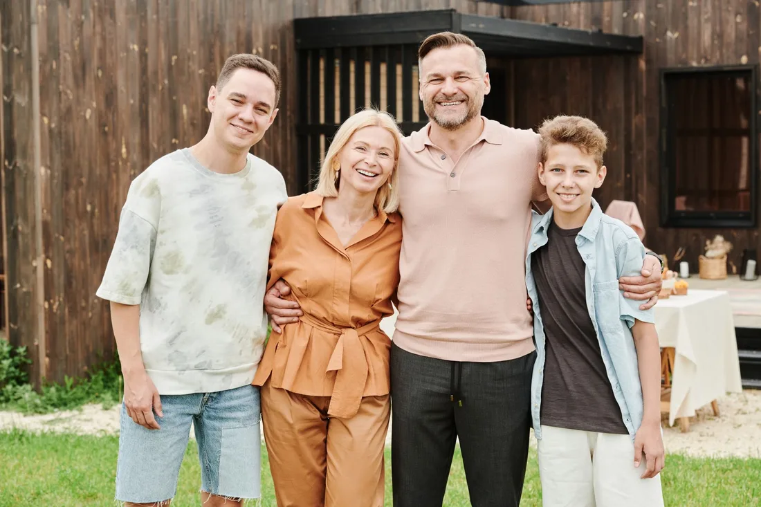 Smiling family of four standing together with arms around each other outdoors. Photo by Julia M Cameron on Pexels
